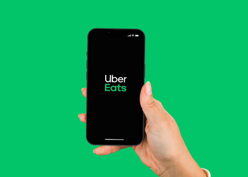 Female hand holding a smartphone iPhone 13 Pro with Uber Eats app on the screen Green background Rio de Janeiro RJ Brazil January 2022 - Tradeinfo.cz Uber Eats