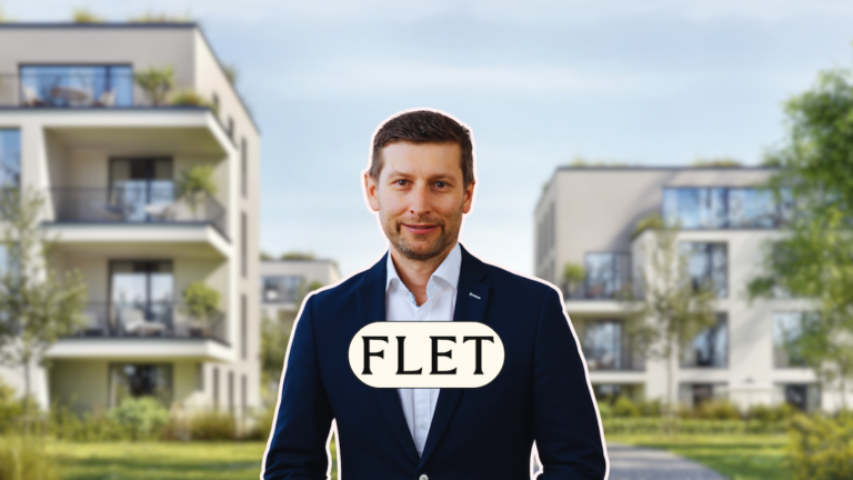 Man in a navy suit posing outdoors in a modern apartment complex with a FLET badge on his chest.