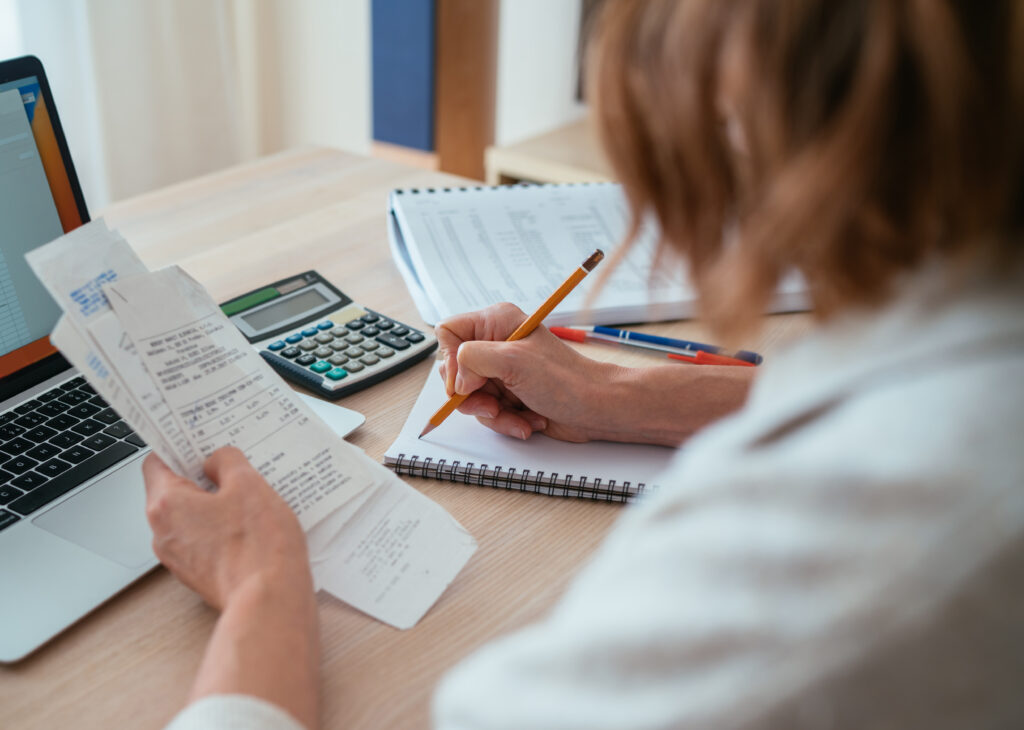 Woman checking paper bills while calculating expenses at home Over-shoulder view of pencil and calculator Home budget smart money management and personal finance planning concept - Tradeinfo.cz money management