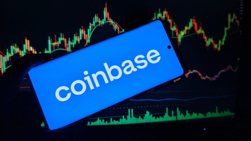 oplus_2097152 - Tradeinfo.cz Coinbase logo on a blue smartphone screen held over a colorful stock/crypto chart in the background.