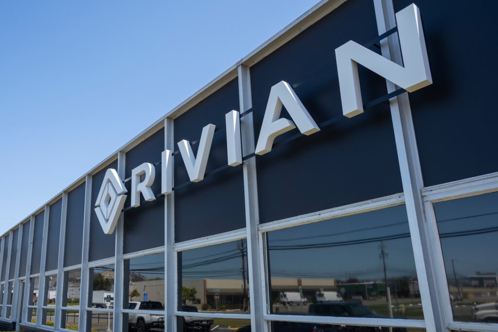 rivian - Tradeinfo.cz Exterior storefront with large white 3D letters spelling 'ARRIVAL' on a dark facade under a clear sky.