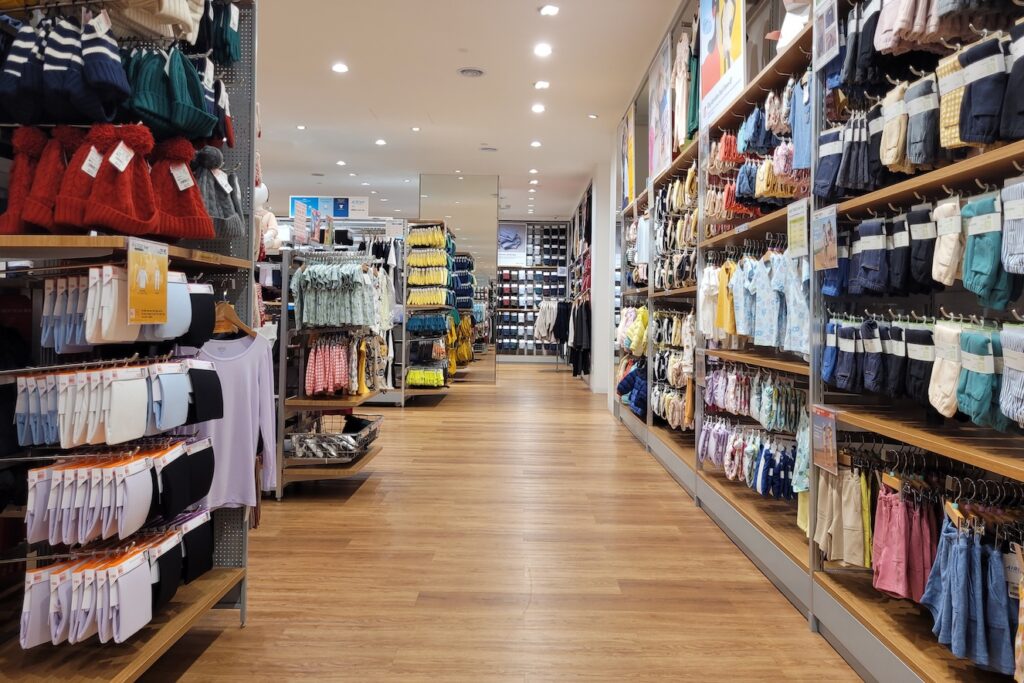 uniqlo 2 - Tradeinfo.cz Bright clothing store aisle with shelves full of colorful socks and hats on both sides, under bright ceiling lights.