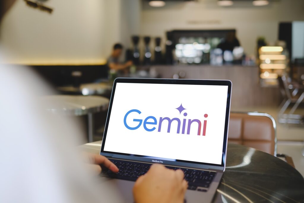 Gemini - Tradeinfo.cz Laptop on a cafe table showing the Gemini logo on a white screen