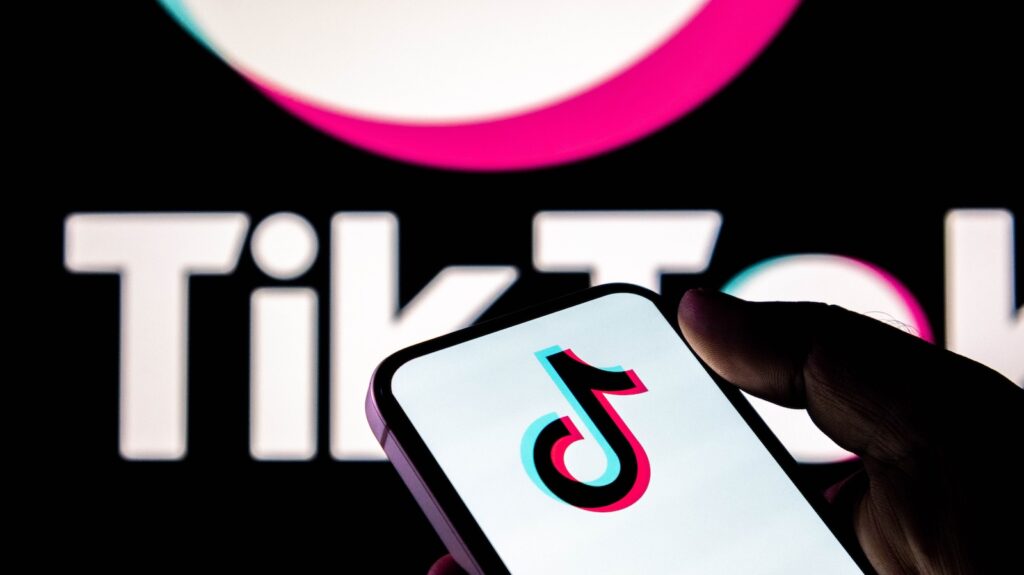 TikTok - Tradeinfo.cz Person holding a smartphone displaying the TikTok logo, with the TikTok wordmark blurred in the background.