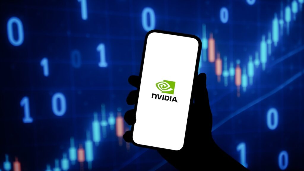 NVIDIA logo displayed on a smartphone screen Delhi India June 04 2025 - Tradeinfo.cz Hand holding a smartphone showing the NVIDIA logo against a blue digital background with 0s and chart candlesticks (tech/finance theme).