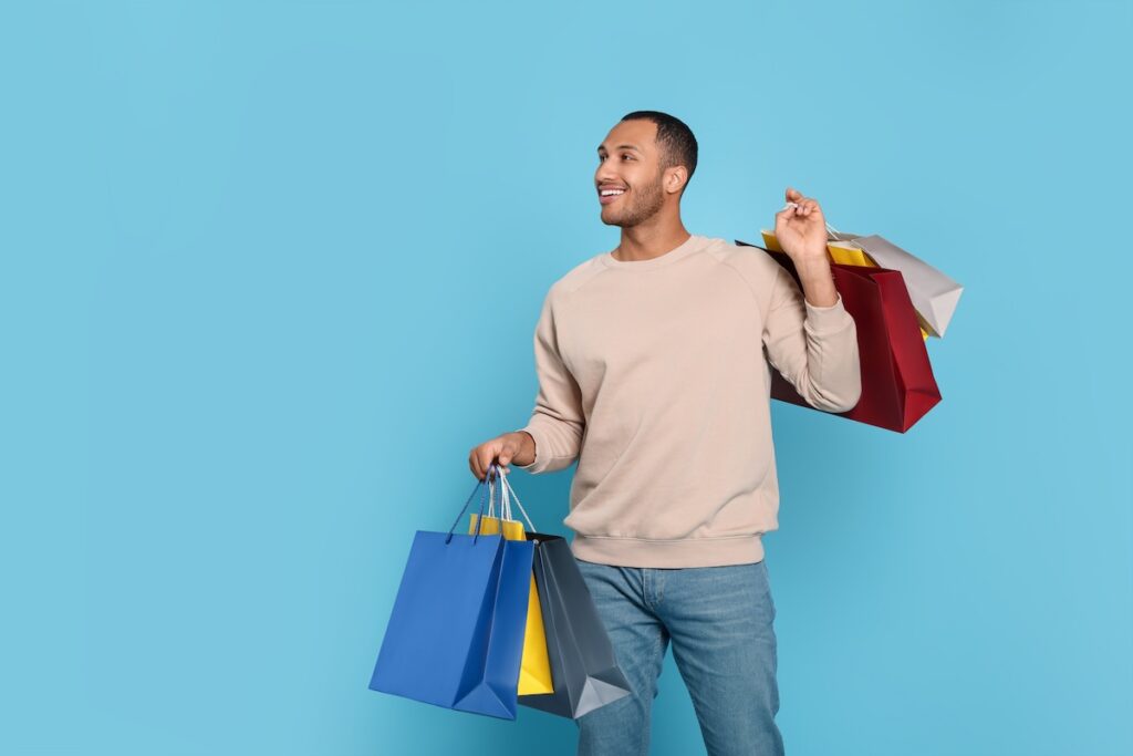 Happy African American man with shopping bags on light blue background - Tradeinfo.cz Action v Česku
