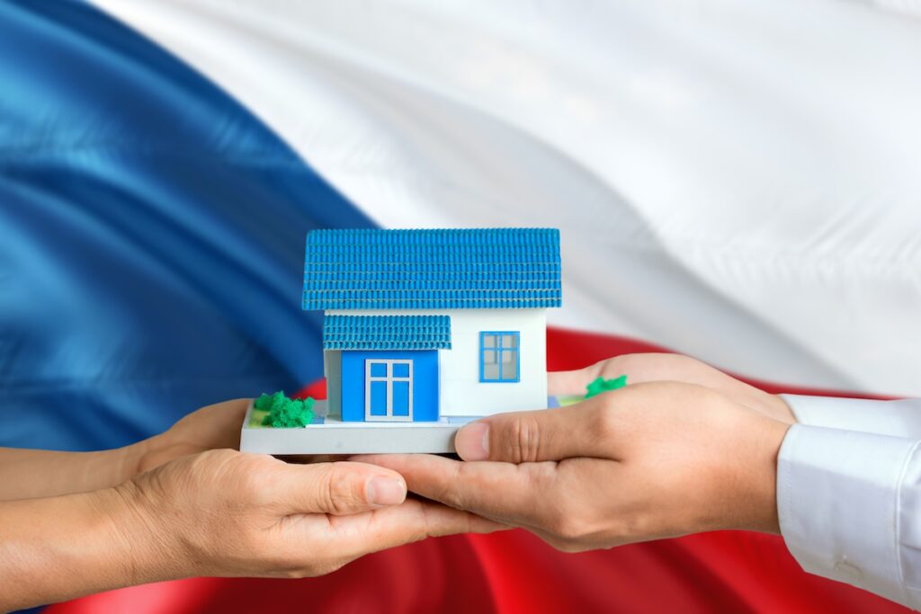 nemovistostiČR - Tradeinfo.cz Small model house held gently between two hands, symbolizing housing support or ownership.